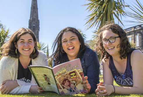 Hailey Austen, Rachel Davis, and Grace Wright outside with one of their comics.