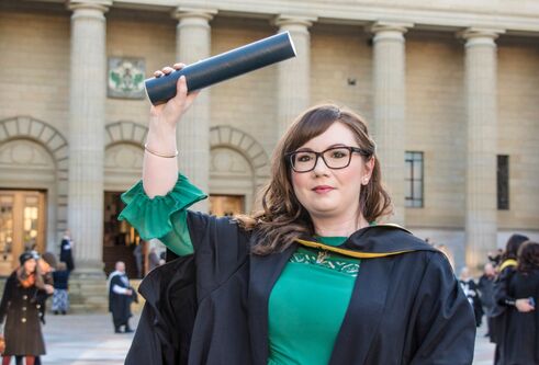 Photo of Aimee Hutchinson outsite Caird Hall wearing her graduation gown and waving her degree about