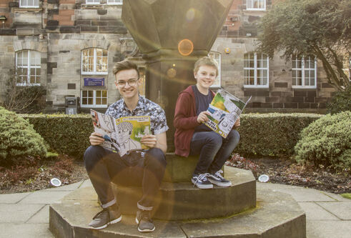 Drew Marr sitting in the University's quad holding a comic