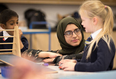 A teacher helping students use a model of a wooden ramp