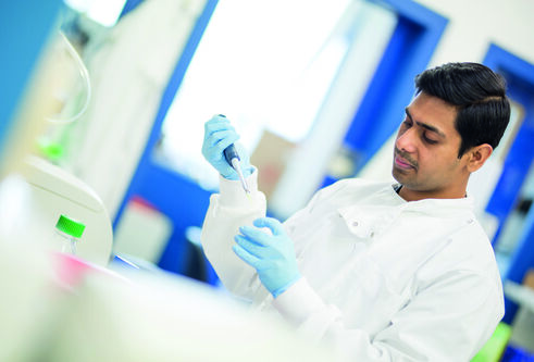 A man in a lab coat with gloves holds a pipet