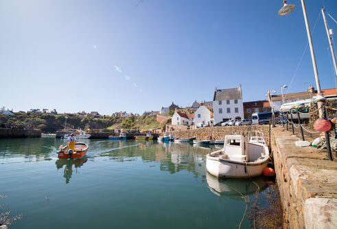 A small fishing boat comes into Crail Harbour, surrounded by buildings from the 17th-19th century