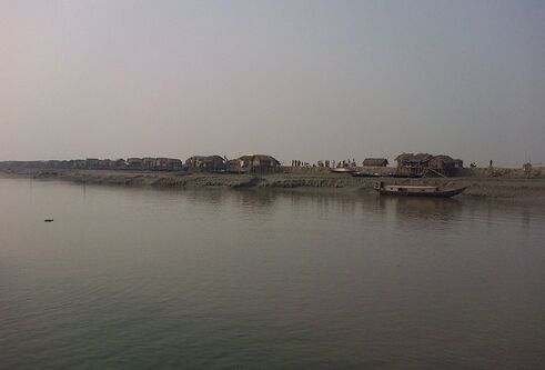 grey looking river with traditional houses alongside it in Bangladesh