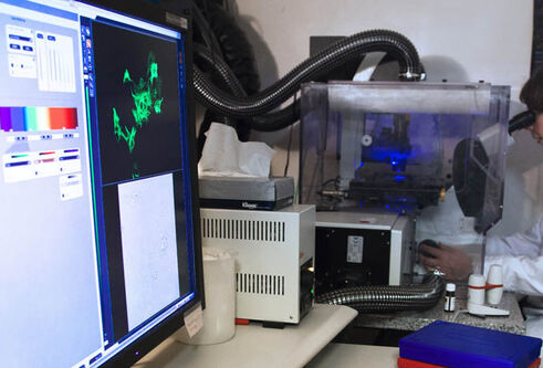 A person in PPE looking through a microscope