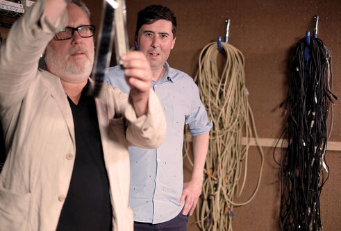 2 men examining something with ropes hanging on the wall behind them 