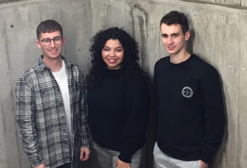 Three students standing before a concrete wall