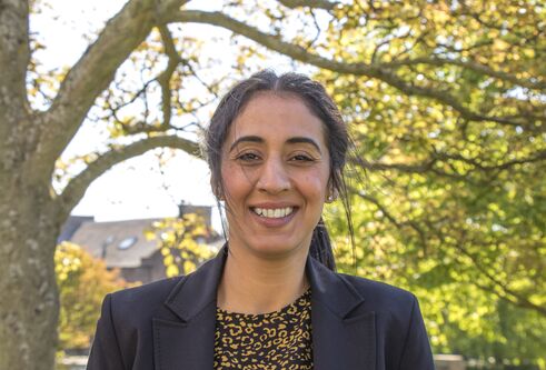 Norin Arshed standing smiling to the camera with a tree behind her