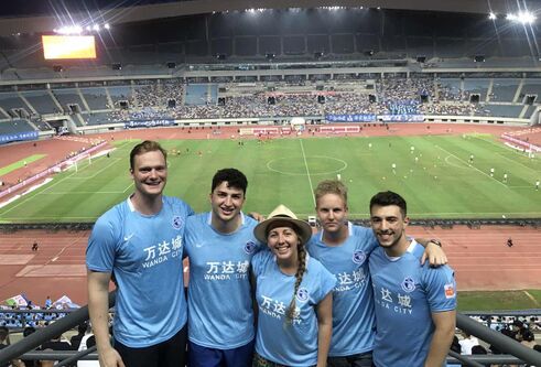 5 people in blue football kits with a footfall stadium behind them 