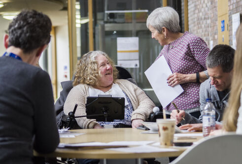 Female User Centre participant who uses communication device for speaking in conversation with volunteer during a group session.