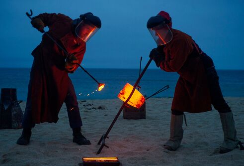 people on beach with sticks with molten metal on the end for bell casting
