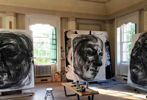 Canvases with heads painted on them, stacked up around a bright gallery
