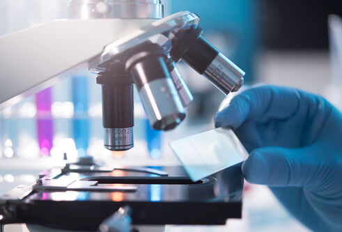 a close shot of a microscope with a gloved hand holding a glass slide