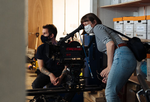 Rose Hendry, wearing a face mask, operates a film camera on tracks.