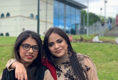 Falak and Suman standing on grass in front of a building with lots of glass