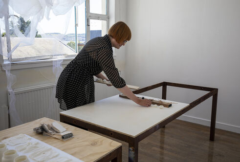 Mhairi Wilde in a studio setting leaning over a table and placing objects in a line