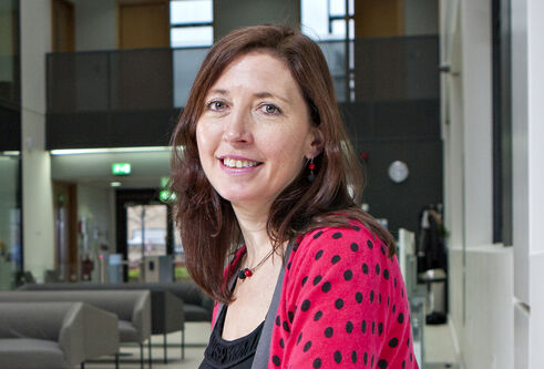 woman sitting in area with sofas, wearing a bright red cardigan with black spots