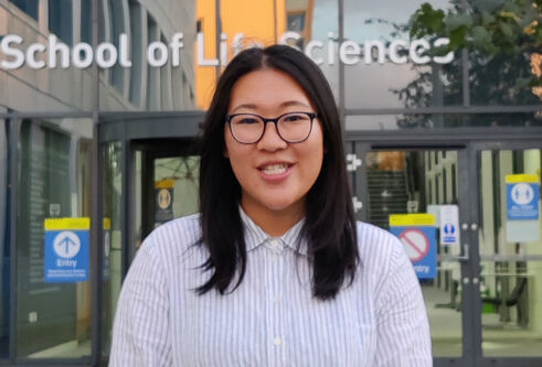 portrait of Vivien Shek in front of modern building, wearing a lab coat
