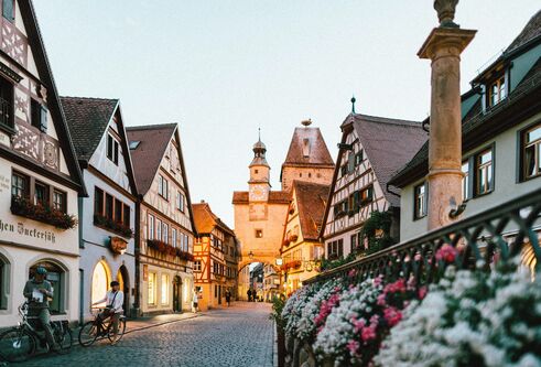 A medieval Bavarian town centre with flowers and people on bikes in Bavarian dress.