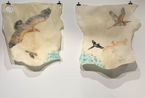 two roughly cut pieces of light fabric with flying birds drawn on them, hanging on white wall