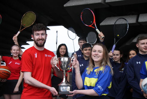 a young man in his 20's, holding half of a large silver trophy while a young woman of similar age holds the other half