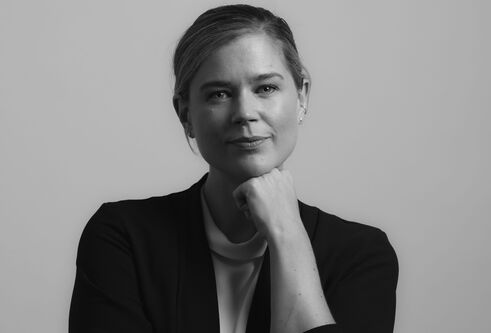 Sheryl Bartlett poses with hand under chin wearing black jacket against a plain background, in grayscale image.
