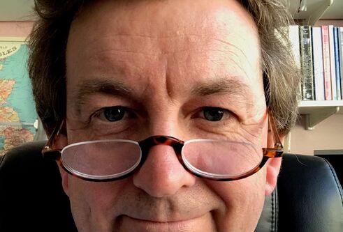 Bespectacled man smiling in front of bookshelves
