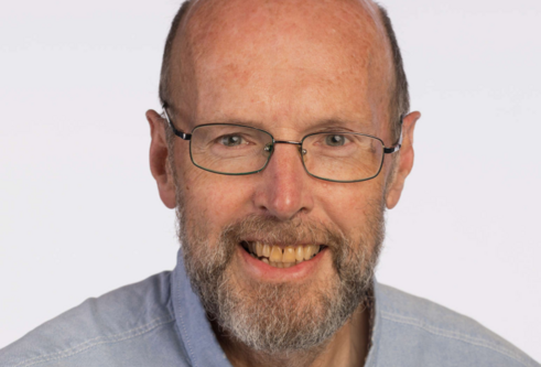 head shot of man wearing light blue shirt and thin glasses