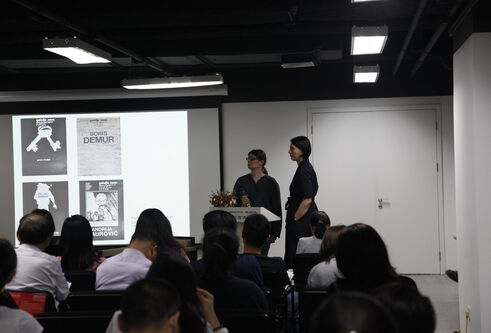 Two speakers stand at a podium in a room full of people.
