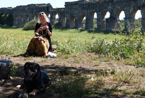 Fiona McHugh sitting in a field with an old acquaduct in the background and a dog at her feet