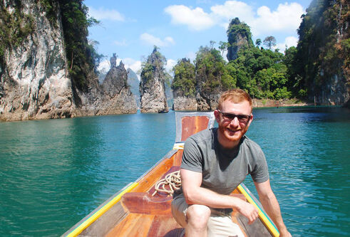 Ricardo Grammatica sits in a boat in a tropical location. Rocky cliffs and trees are in the background.