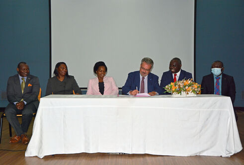 Principal Iain Gillespie sits at the centre of a table with a white table cloth. He is flanked by five representatives from Malawian universities as he signs an agreement.