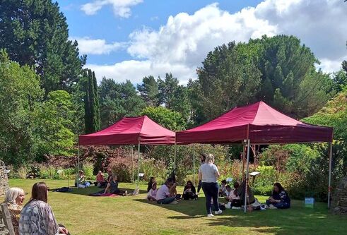 People sit under two red gazebos surrounded by trees.
