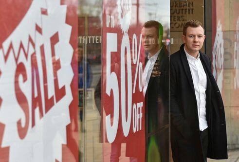 Cally Russell stands with his back to a shop window displaying red sale signs.