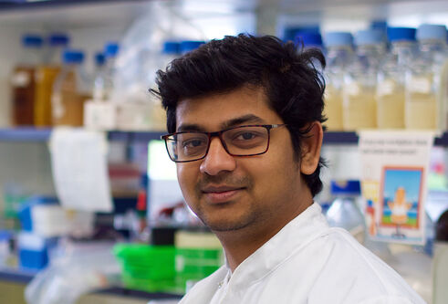 Joshua Peter standing in a lab with shelves full of bottles and lab equipment behind him