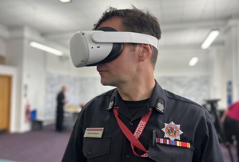 A man from the Scottish Fire and Rescue Service stands with a white VR headset mounted on his head