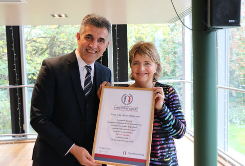 Wendy Alexander holding the framed University of Sanctuary award with a representative from City of Sanctuary