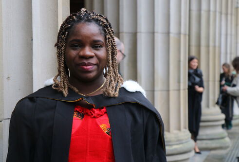 Martha, wearing graduation robes, stands outside the Caird Hall