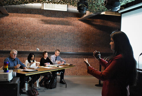 A speaker standing in front of a panel of four judges giving a talk