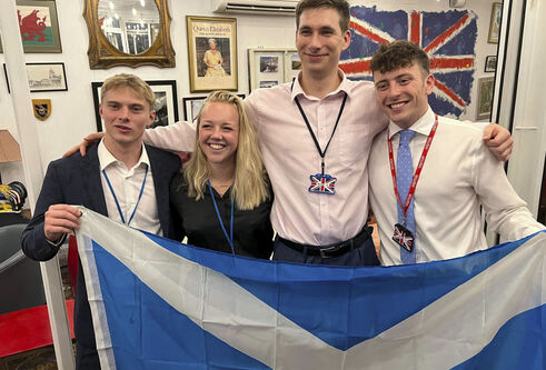 Four people stand together smiling, holding up the Scottish flag.