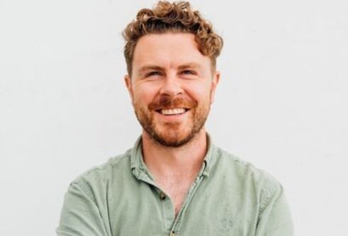 Alan is stood in front of a white background wearing a light green shirt. He's standing with his arms crossed, smiling into the camera.