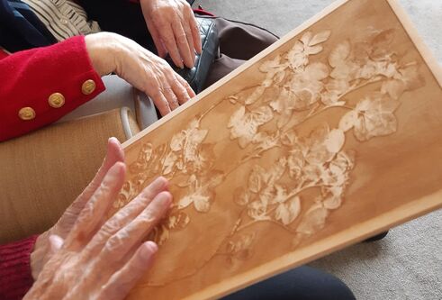 Photo of a seated person's hands holding a embossed wooden image.