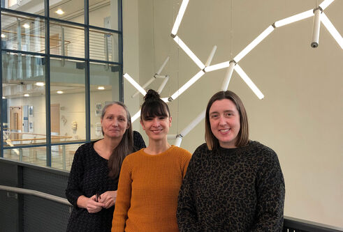 Kate, Aida, Gail standing at a balcony in Life Sciences with a DNA light fixture behind them