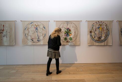 A female looks at a row of tapestries on the wall.