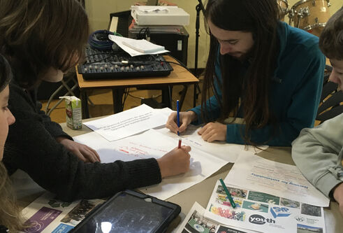 A group of four people sitting around a desk, working collaboratively, writing on pieces of paper.