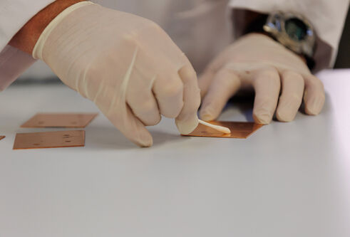 Close up of two gloved hands swabbing a small square copper plate.