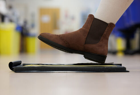 Side view of a woman’s boot held mid-air over an ink pad which is used to record footwear mark forensic evidence.