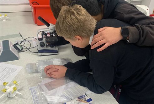 Photograph of S1 students at Baldragon Academy huddled together inspecting the fibres collected from their jumpers.