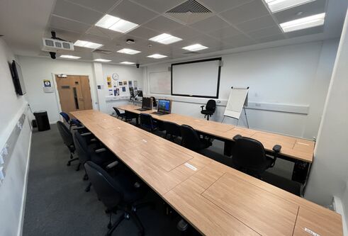 Dalhosuie 1LG02 showing two rows of desks and chairs. PCs are set inside the tables.  with a white screen on the wall