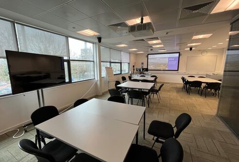 Dalhousie 1G10 - a room with several desks pushed together to form a square table with surrounding chairs and a tv screen and white screen at the far end