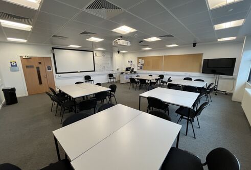 Dalhousie 1S05 - four sets of square tables surrounded by chairs with a tv screen in the corner and a white screen at the front of the room